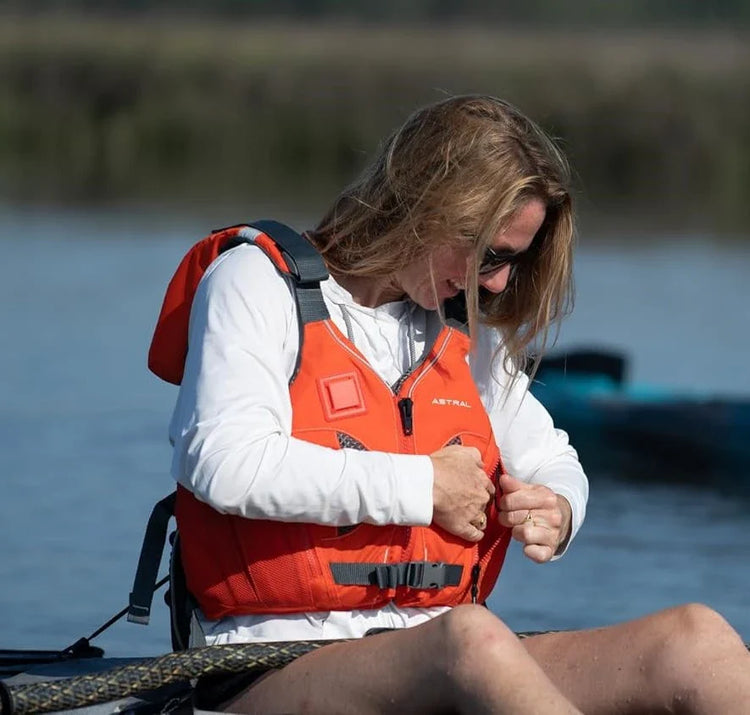 Astral EV-Eight PFD worn by a female kayaker as she inserts her cell phone into the side pocket of the PFD